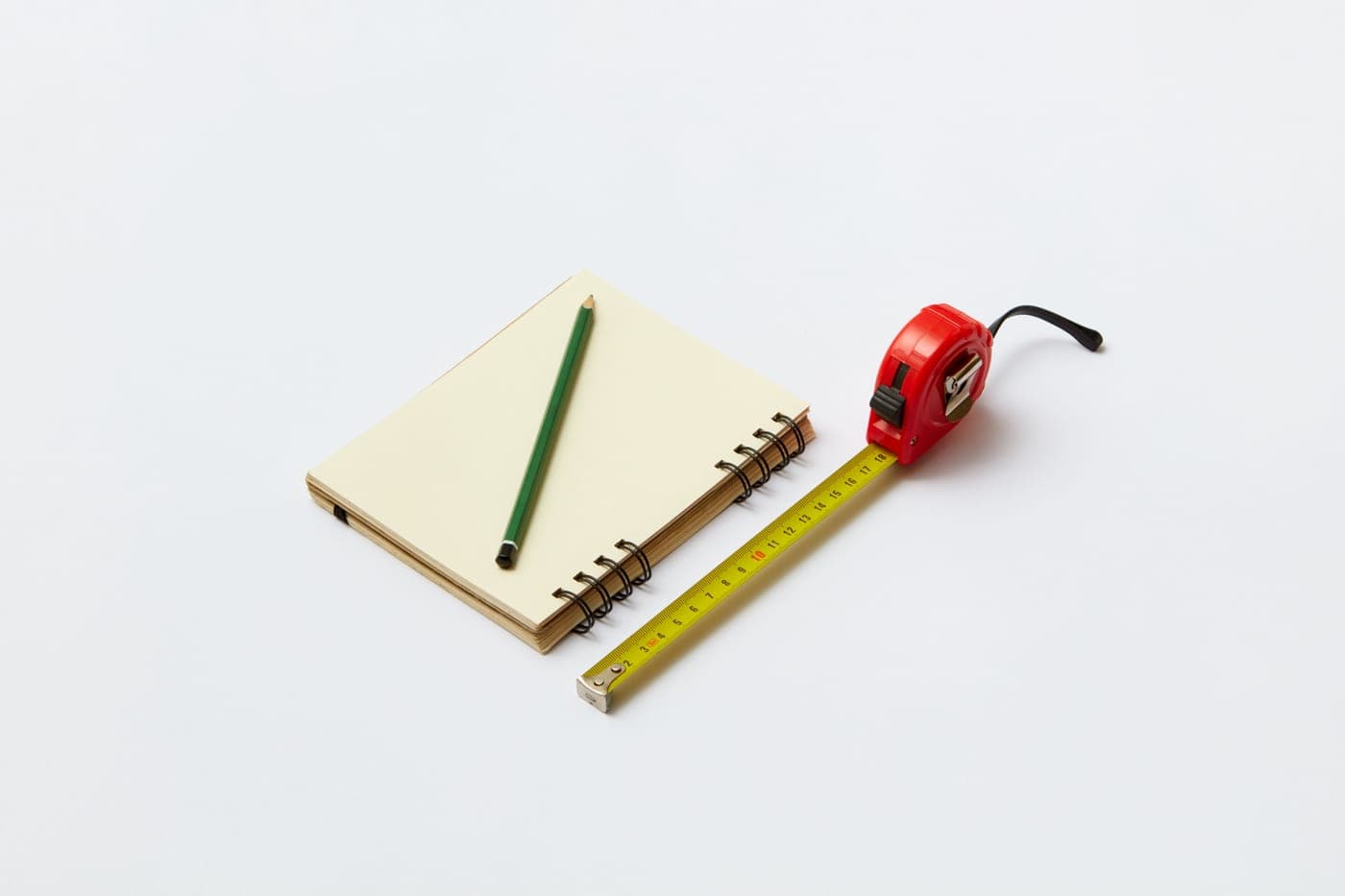A notebook and tape measure on a table beside a lit desk lamp