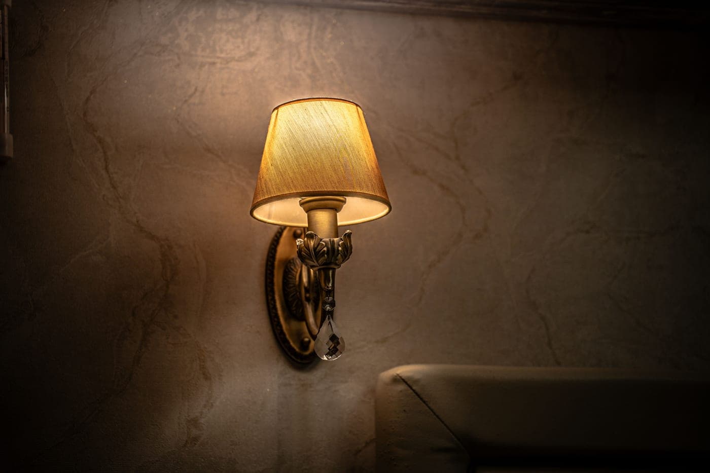 A wall sconce mounted beside a bed with its cord running down to a wall outlet